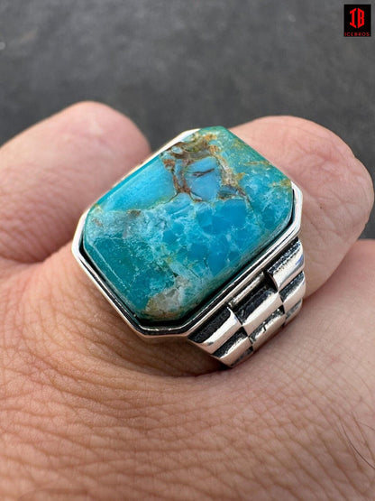 A man's hand holds a ring with a turquoise stone, showcasing its vibrant blue-green color and elegant design.