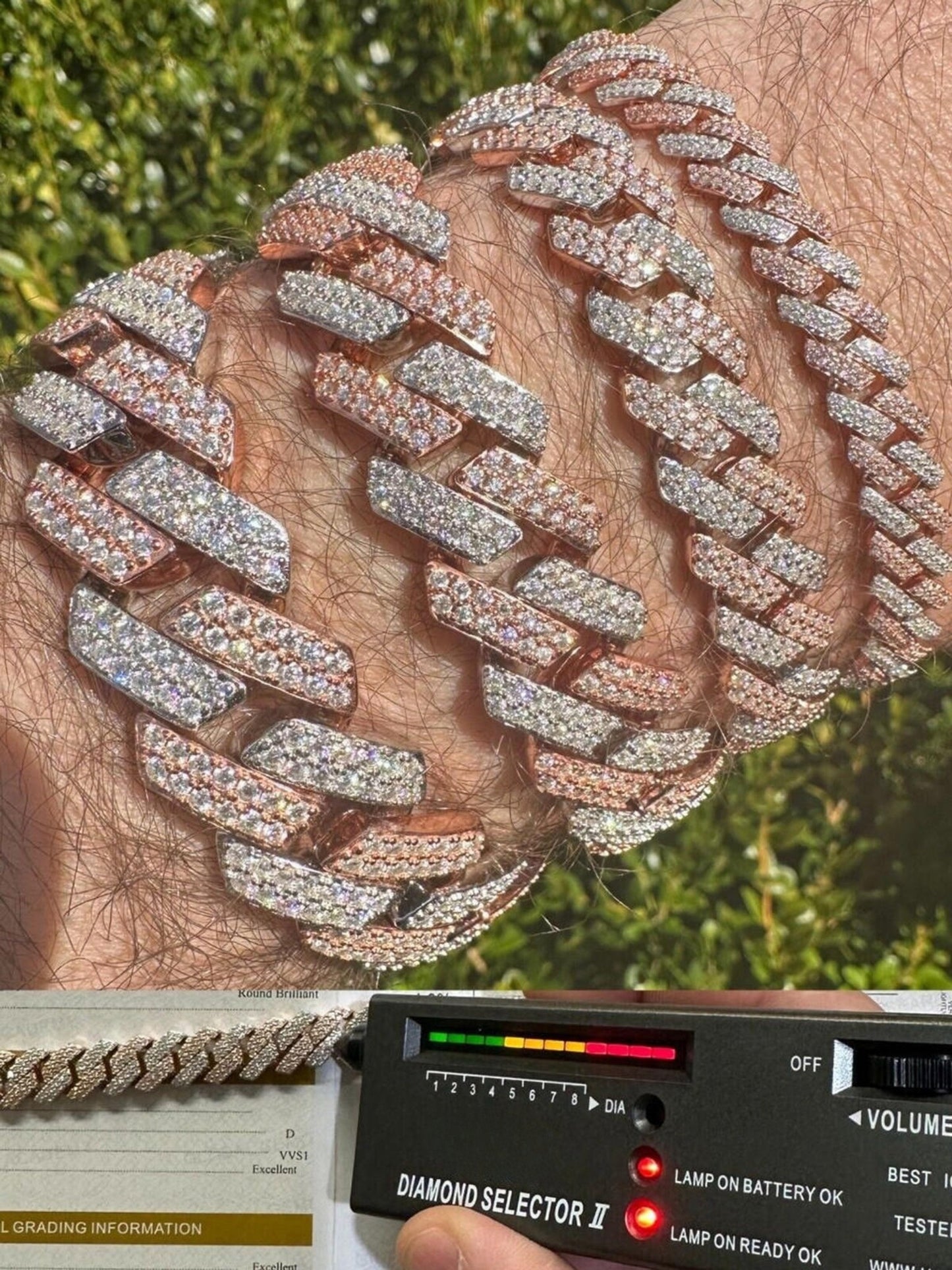 A close-up photograph of a 14k Rose & White Gold Iced out Prong Miami Cuban Link Bracelet being verified by a diamond tester. The bracelet shines with a luxurious mix of rose and white gold, adorned with an array of glistening diamonds. A hand holds a diamond tester against one of the links to confirm the authenticity of the diamonds, creating a moment of assurance and trust in the quality of the jewelry