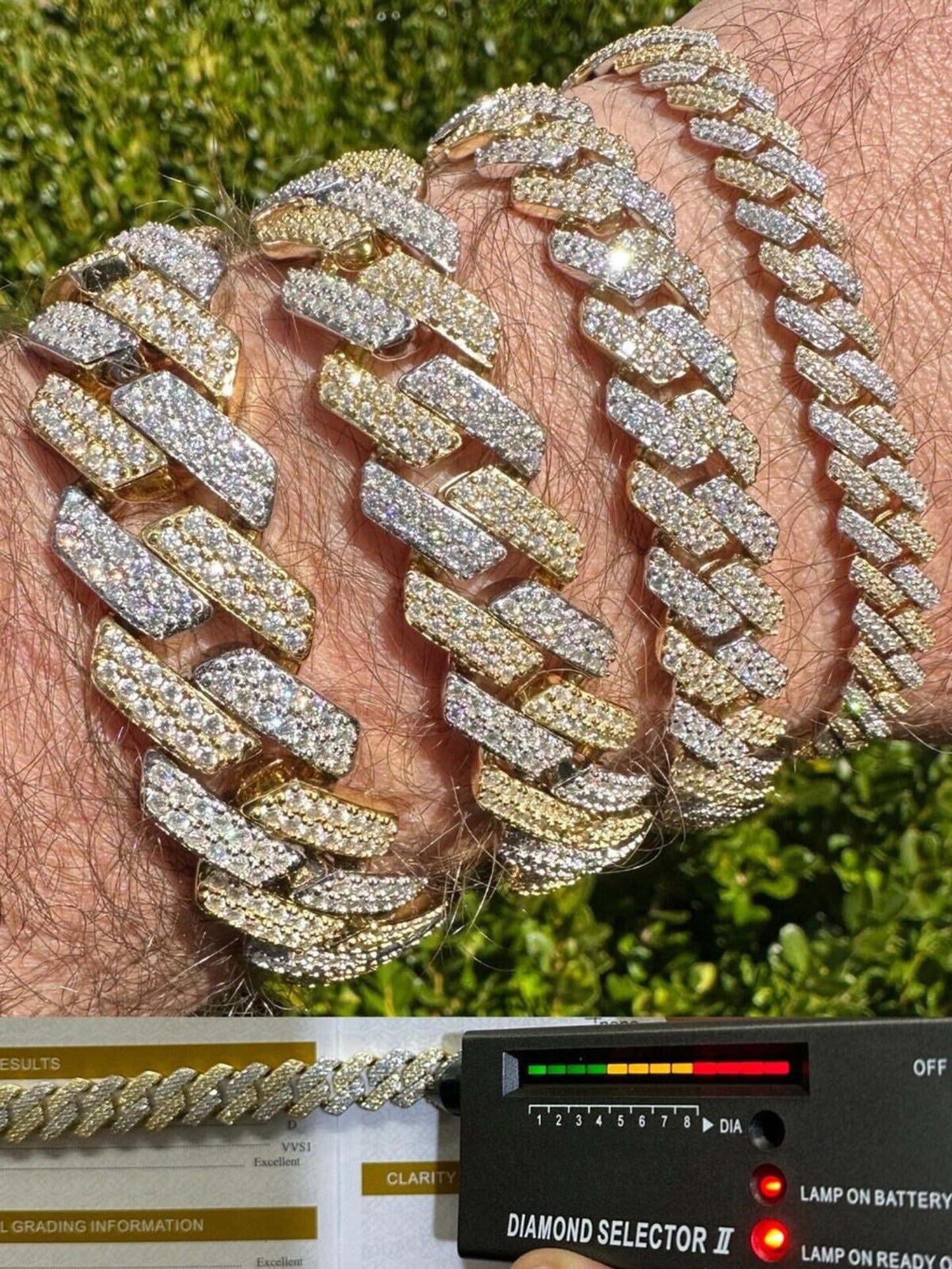 A close-up photograph of a 14k Yellow & White Gold Iced out Prong Miami Cuban Link Bracelet being verified by a diamond tester. The bracelet shines with a luxurious mix of Yellow and white gold, adorned with an array of glistening diamonds. A hand holds a diamond tester against one of the links to confirm the authenticity of the diamonds, creating a moment of assurance and trust in the quality of the jewelry