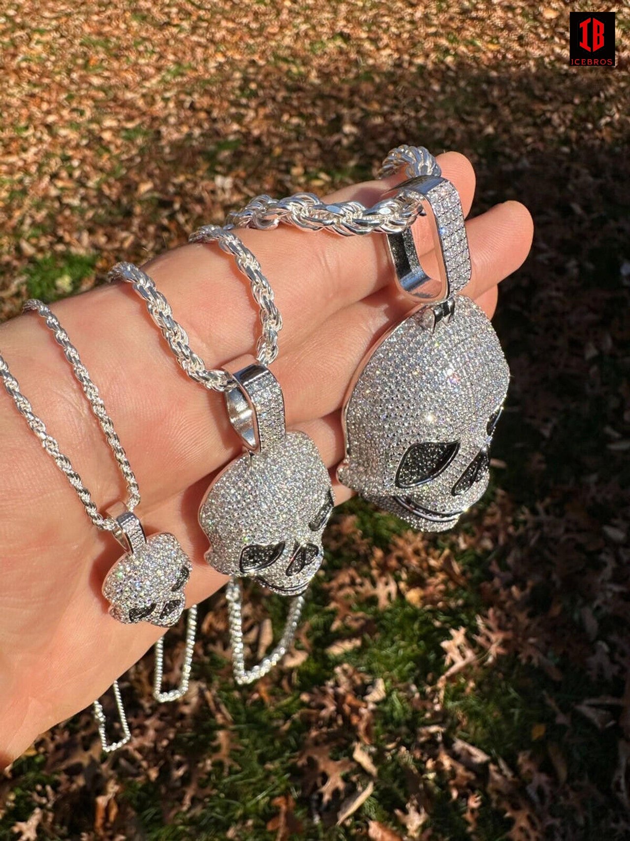 Hand holding three White Gold moissanite skull necklaces of different sizes with 14k White Gold Twisted Rope Chain 